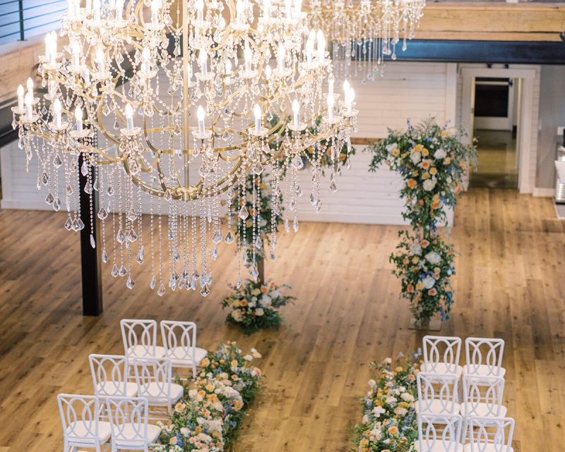 The chandelier hangs above the beautifully decorated aisle, flowers adorn the wedding arch in preparation for the exchanging of vows.