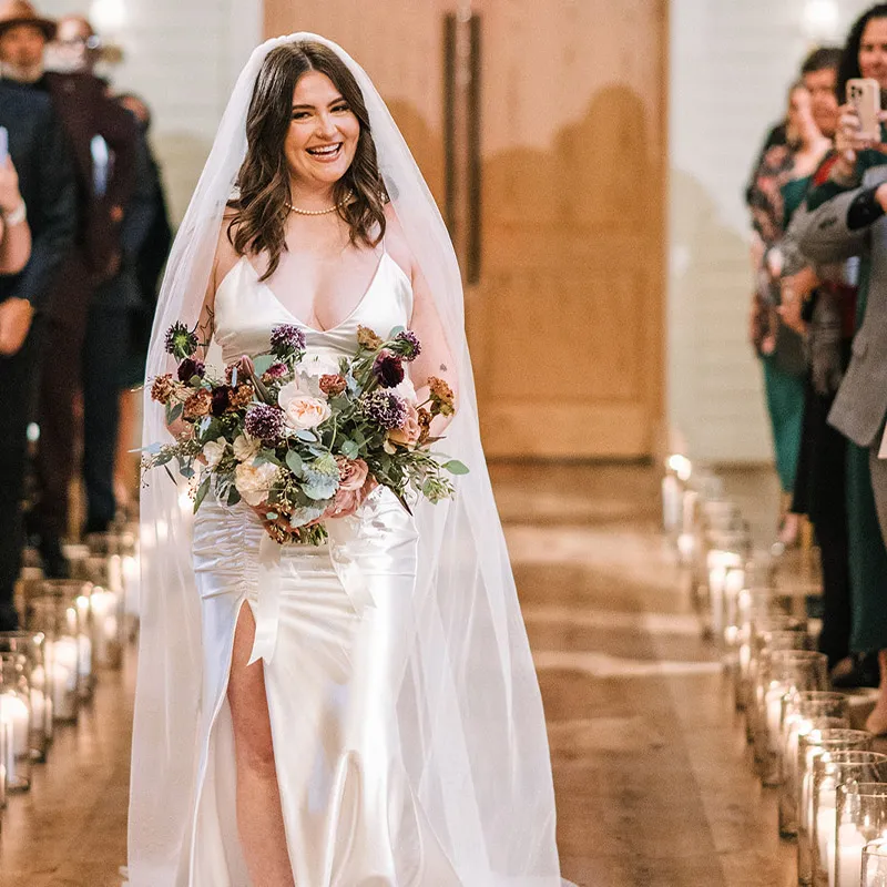 Bride with pearls and a bouquet walks down a candlelit hardwood aisle to married. Brentsville Hall, Manassas, Virginia.