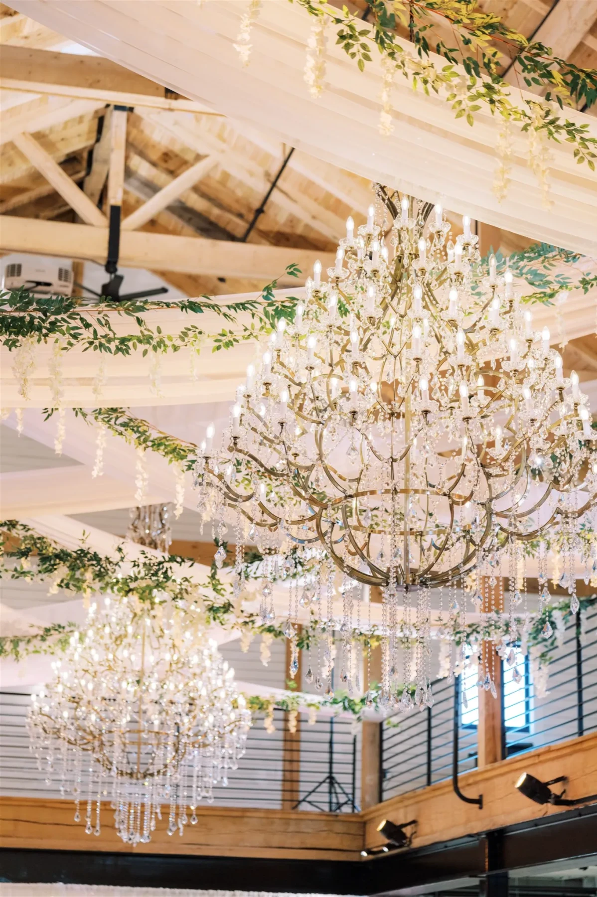 Chandeliers of glass and draped fabric along with greenery hanging from the open rafters of the modern barn at Brentsville Hall